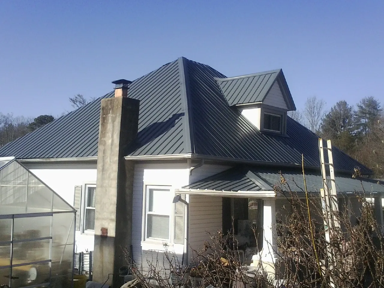 Dark blue standing seam metal roof on a white farmhouse with dormer — Slate & Tile Roof Repair by Roofing Brothers in Morgantown