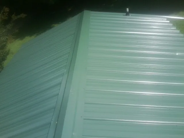 New green metal panels meeting at the ridge of a roof — Flat Roof Repair work by our crew in Morgantown