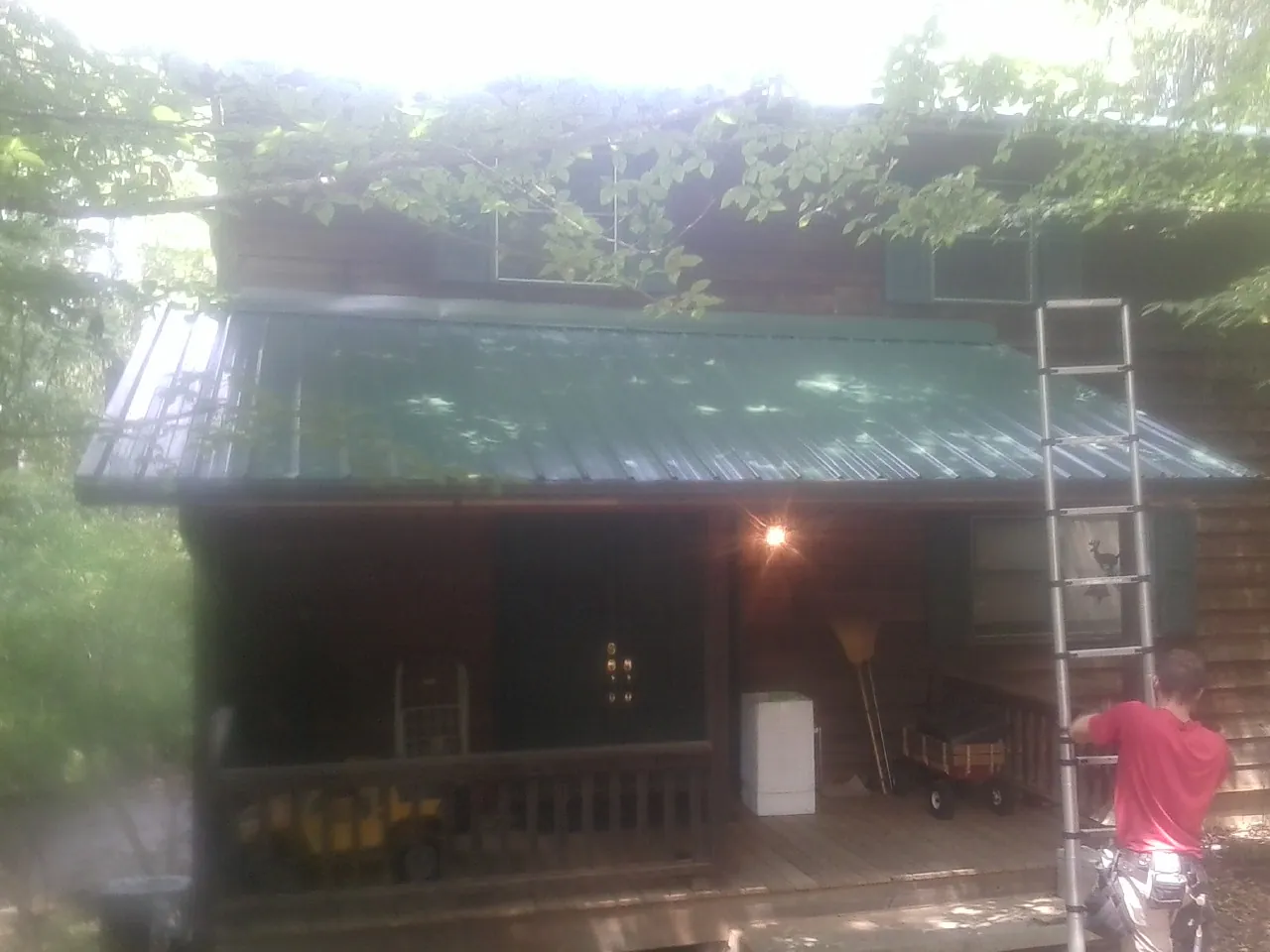 Worker on a ladder at the green porch roof of a wooded cabin in Morgantown