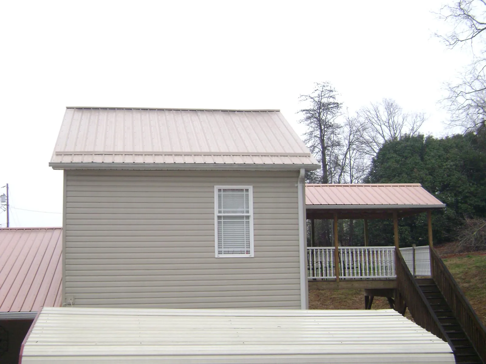 Tan metal roofs on a two story addition and attached porch, from a Roof Replacement job in Morgantown